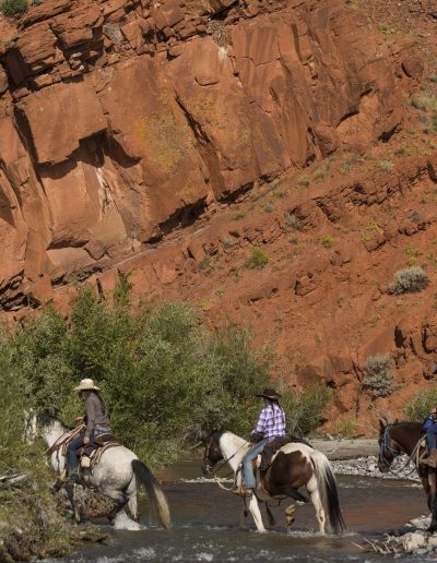 Wrangler and 2 children crossing the East Fork River with a red rock cliff in background - Lazy L&B Dude Ranch Wyoming