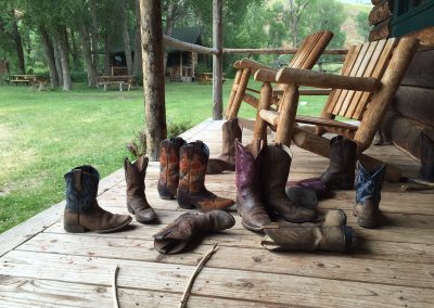 Lots of pairs of kids cowboy boots strewn on front porch of log cabin - Lazy L&B Dude Ranch Wyoming